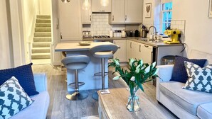 A modern kitchen with white cabinets, a central island with bar stools, a yellow coffee machine, and a staircase leading to another level.