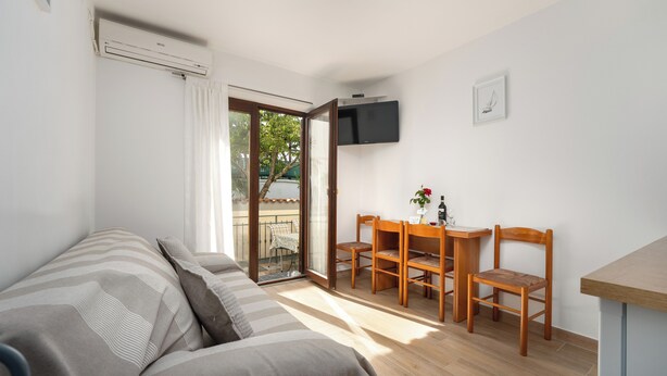 A room with a bed, a desk with two chairs, a TV mounted on the wall, and a sliding glass door leading to an outdoor area. - Funtana Apartments Budinjaš APP 3 FREE BIKES (FUNTANA)
