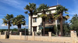 A two-story house with a balcony, surrounded by palm trees. - Funtana Apartments Budinjaš APP 3 FREE BIKES (FUNTANA)