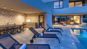 Un espace piscine extérieur moderne, doté de chaises longues et d’un coin repas.
