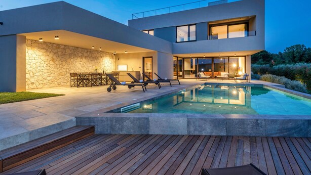 Une maison moderne dotée d’une piscine, d’un espace salon extérieur et d’un mur en pierre.