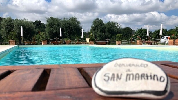 Taula de fusta al costat de la piscina amb un posavasos que diu "BENEVOLTO SAN MARINO".