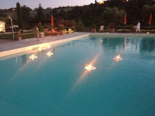 Ein Swimmingpool mit schwimmenden Kerzen, umgeben von Stühlen und Topfpflanzen.
