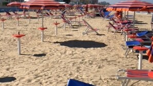 Una platja amb files de gandules i ombrelles, sorra daurada i un edifici al fons.