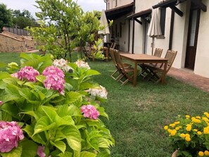 Eine Terrasse mit Holztisch und -stühlen, umgeben von üppiger Vegetation und blühenden Pflanzen.