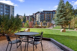 A courtyard with a round table and chairs, surrounded by a well-maintained lawn and a few trees. - Sundial 1BR in the heart of Canyons Village, walk out to pool, private patio, near hiking & biking (Park City)