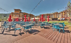 A spacious outdoor dining area with blue chairs and red umbrellas, overlooking a mountainous landscape. - Sundial 1BR in the heart of Canyons Village, walk out to pool, private patio, near hiking & biking (Park City)