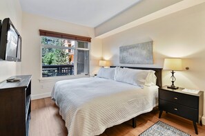 A bedroom with a bed, bedside tables, a TV, a window with blinds, and a view of the outdoors. - Sundial 1BR in the heart of Canyons Village, walk out to pool, private patio, near hiking & biking (Park City)