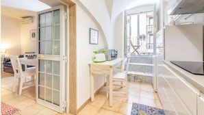 Une cuisine compacte avec un coin repas, une chaise blanche, une petite table avec un four à micro-ondes et un escalier menant à un balcon extérieur.