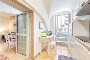 Cocina compacta con comedor, una silla blanca, una mesita con microondas y una escalera que lleva a un balcón al aire libre.