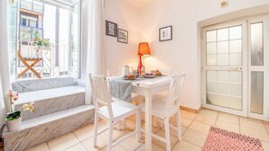 Un coin repas avec une table dressée pour deux personnes, des chaises blanches, une lampe rouge et une petite plante en pot.