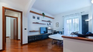 A modern living room with a wooden floor, a sofa, a TV, and a dining area.