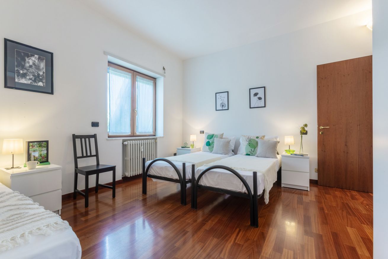 A bedroom with a bed, two bedside tables, a chair, a window, and a door.