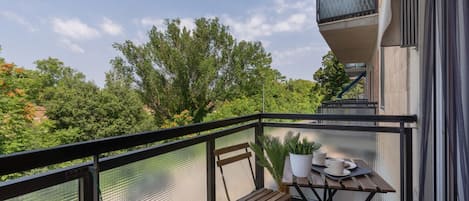 A balcony with a table and chairs, a potted plant, and a view of trees and buildings.