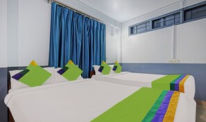 A hotel room with two beds, blue curtains, a window with blinds, and a power outlet on the wall.