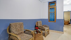 Een kamer met twee rieten stoelen en een kleine tafel, een blauw-witte wand en een raam met blauwe gordijnen.