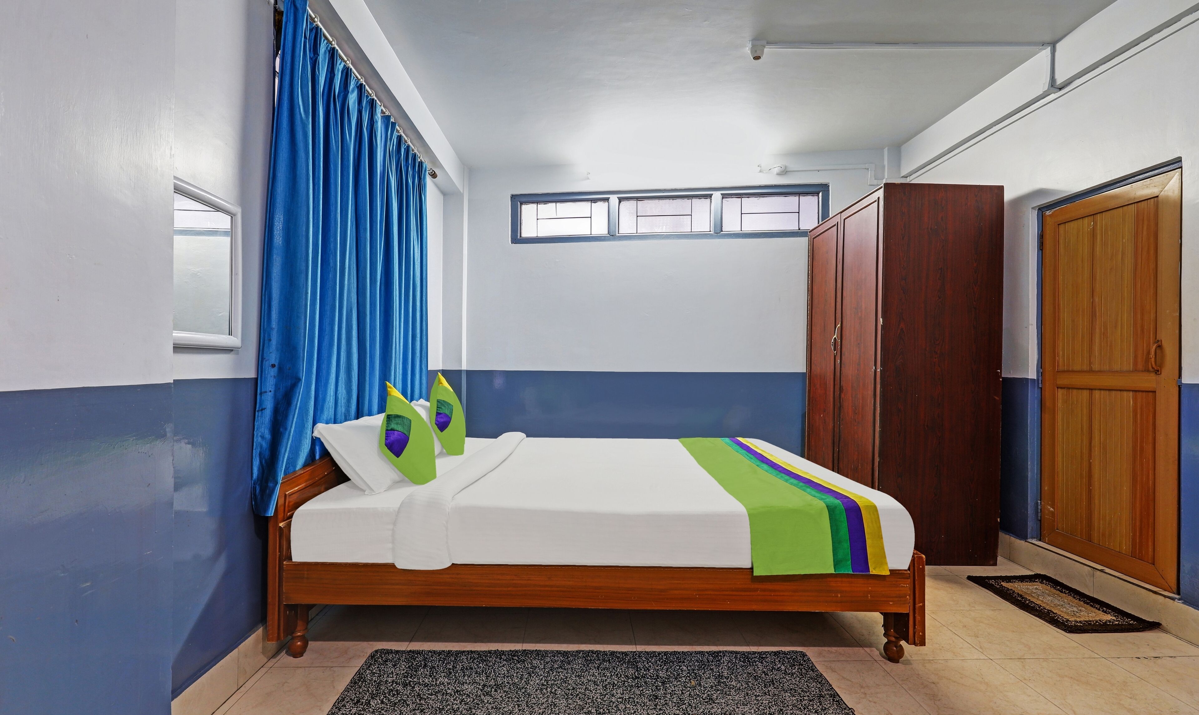 A bedroom with a wooden bed, blue curtains, a wardrobe, and a window with blinds.