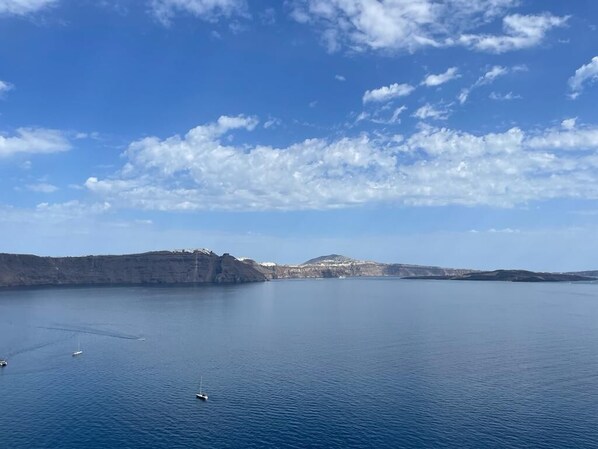 A calm sea with boats and a mountainous coastline under a clear sky.