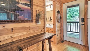 A wooden interior with a bench, a door leading outside, and a mirror reflecting a bathroom with a sink and towel rack. - Rustic Young Harris Cabin w/ Fire Pit & Views (Young Harris)
