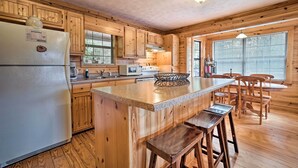 A kitchen with wooden cabinets, a refrigerator, a countertop, and a dining area with chairs. - Rustic Young Harris Cabin w/ Fire Pit & Views (Young Harris)