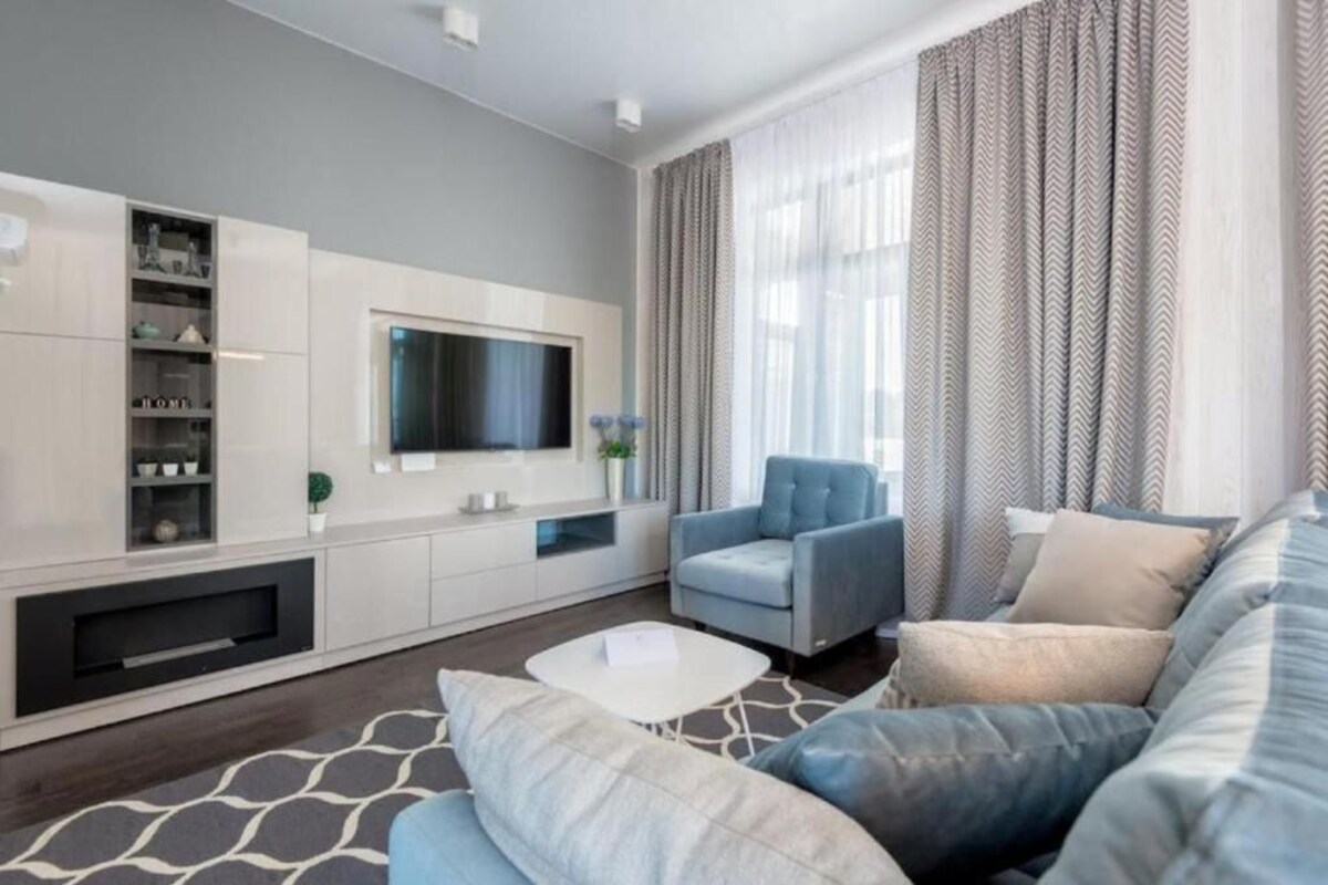 A modern living room with a sofa, armchair, and a flat-screen TV mounted on the wall.