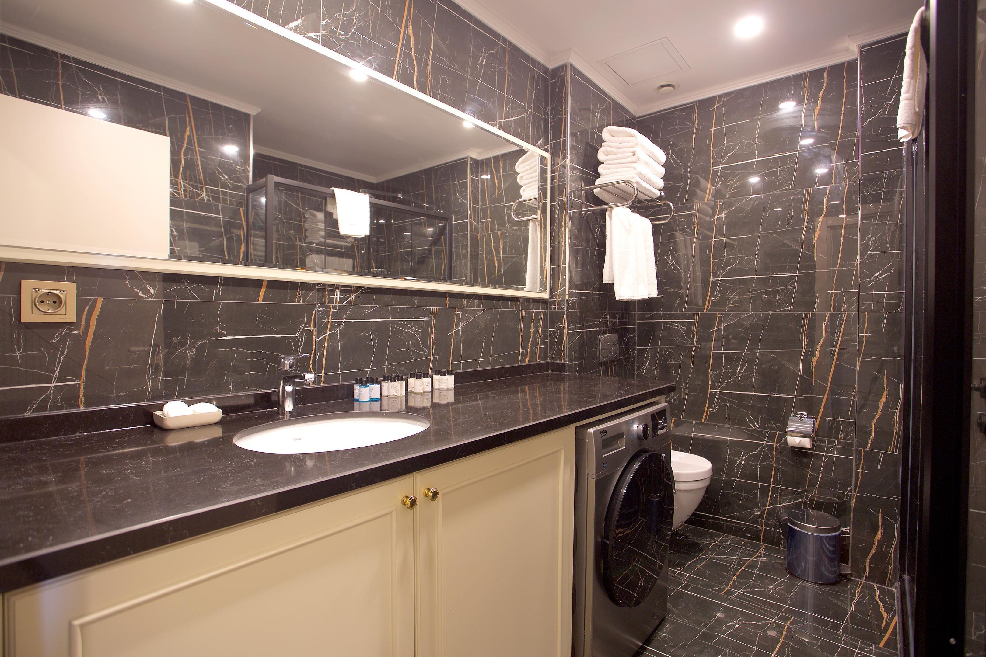 A modern bathroom with a marble vanity, a sink, a mirror, a washing machine, and a toilet.