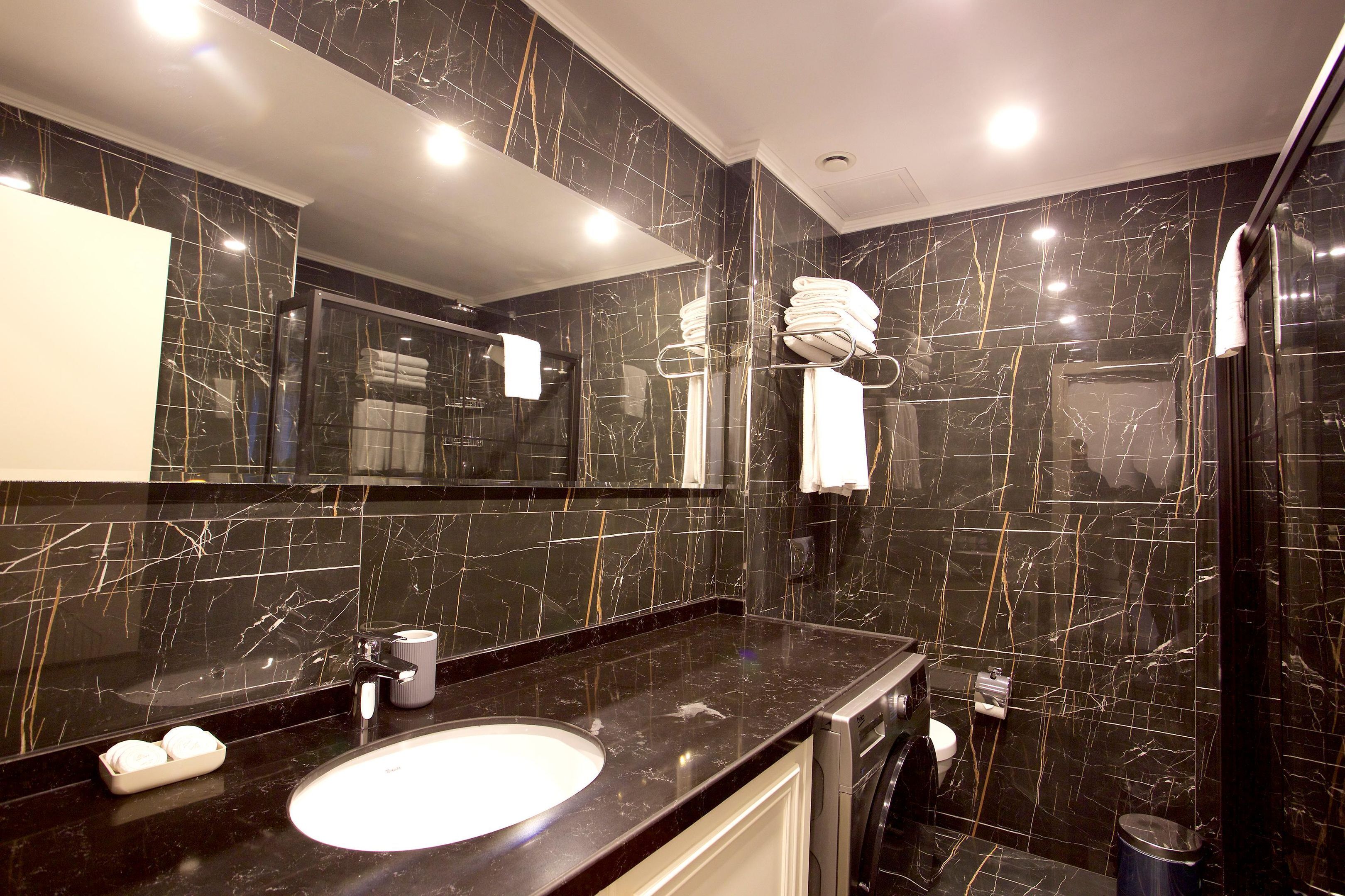 A modern bathroom with a black marble sink, a large mirror, and a glass shower enclosure.