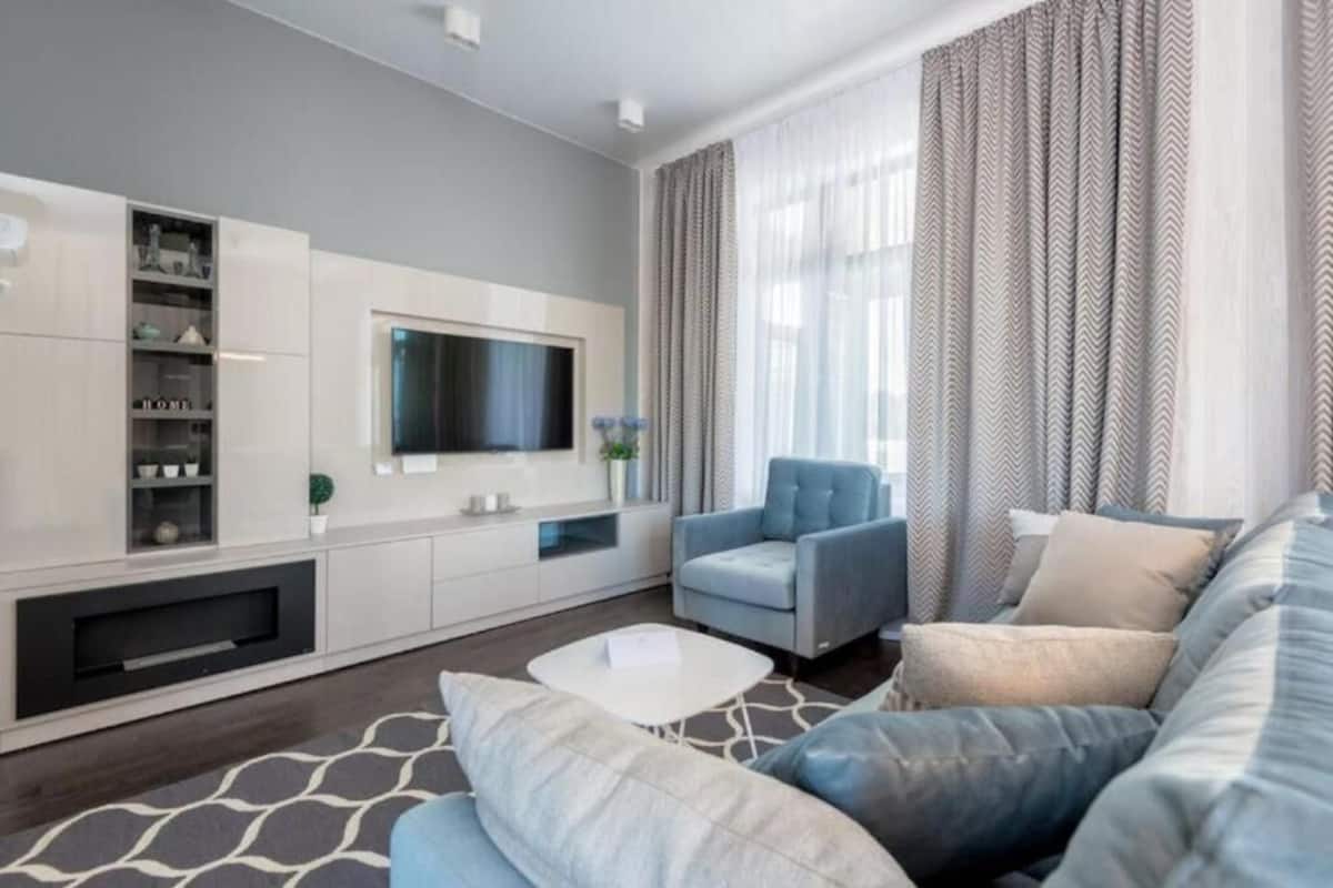 A modern living room with a sofa, armchair, and a flat-screen TV mounted on the wall.