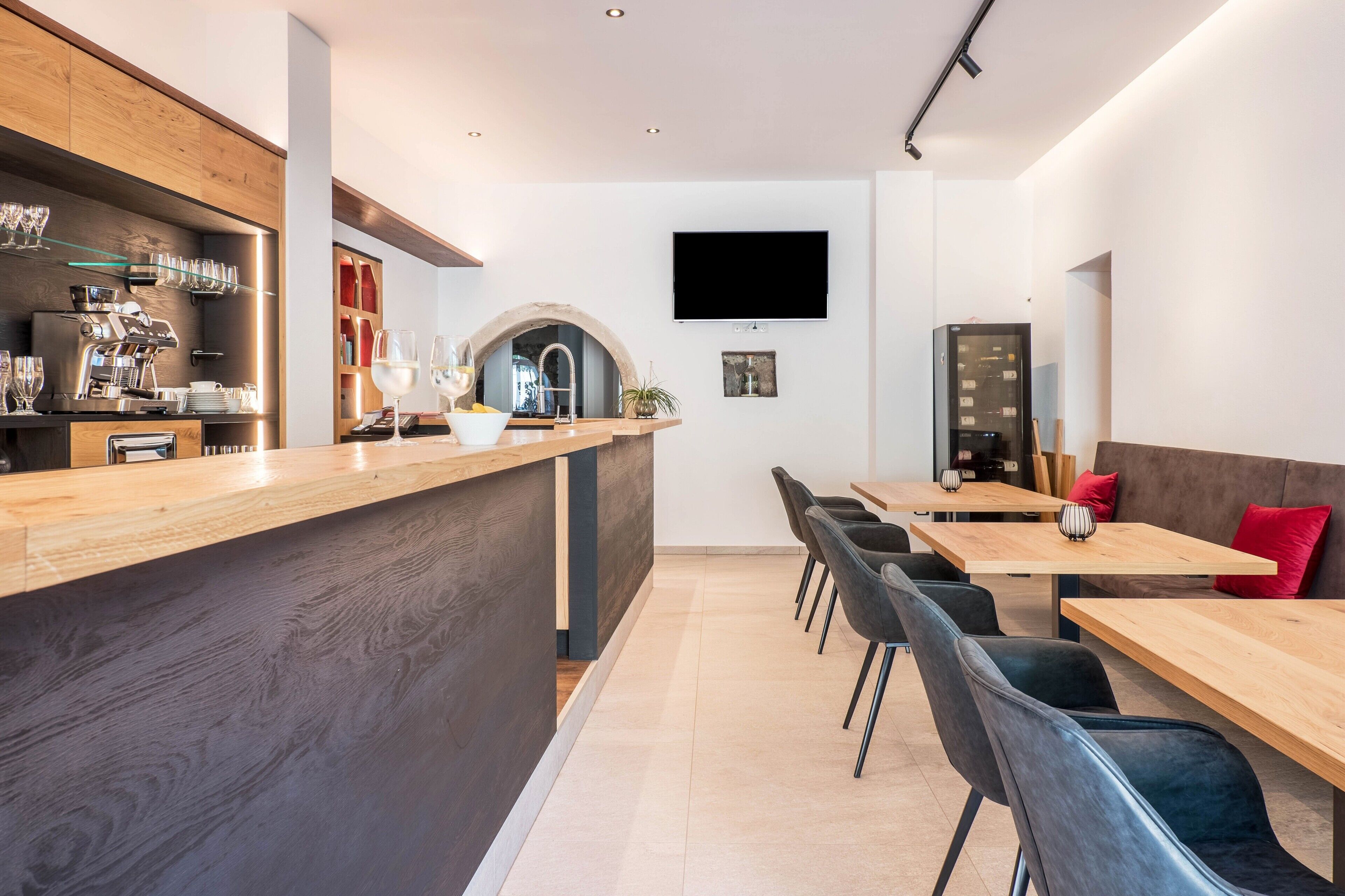 A modern kitchen with a wooden bar, a flat-screen TV, and a dining area with black chairs and a wooden table.