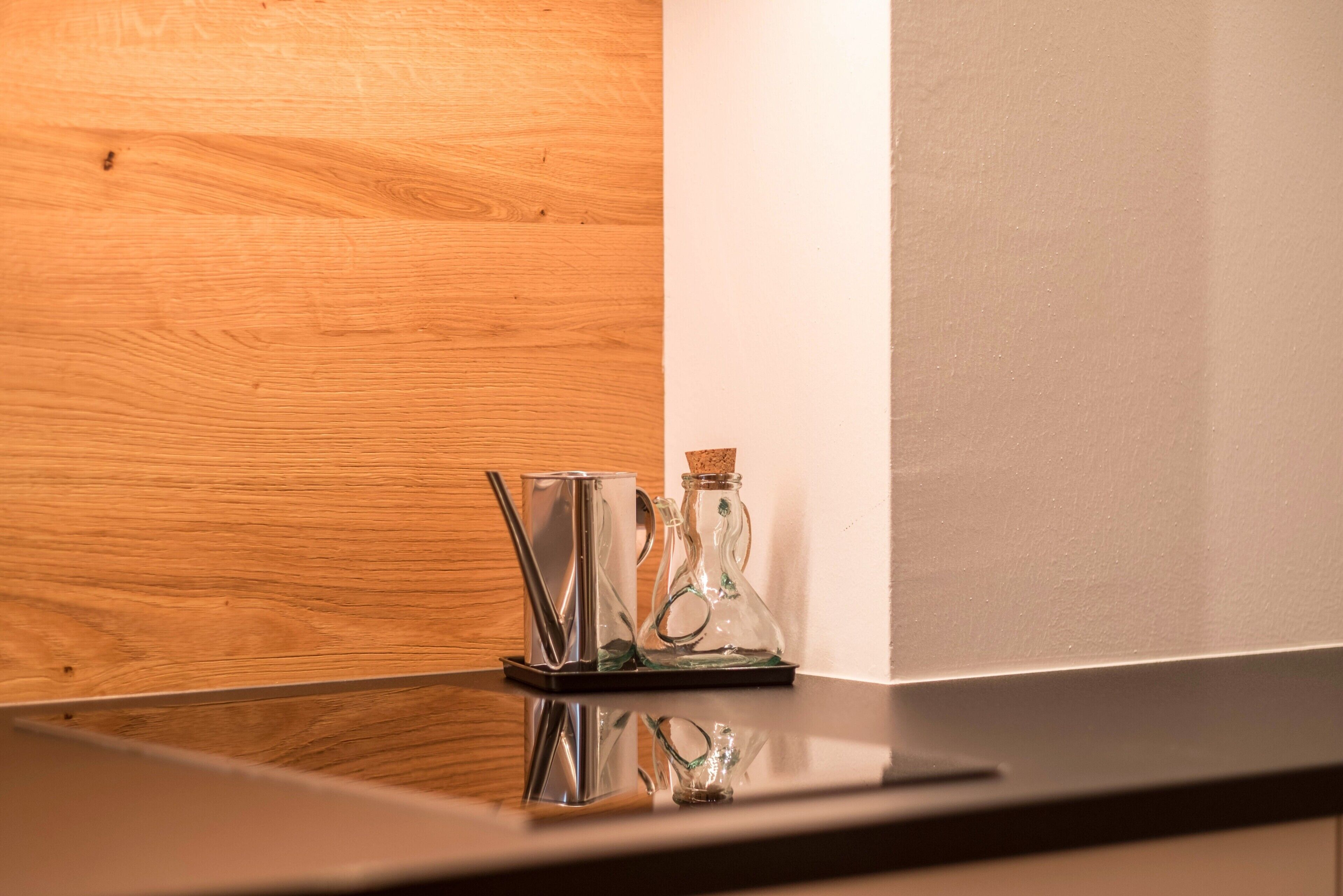 A wooden wall and a reflective surface with a glass bottle and a metal cup.