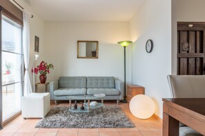 A living room with a sofa, a coffee table, a lamp, a clock, and a view through a window.
