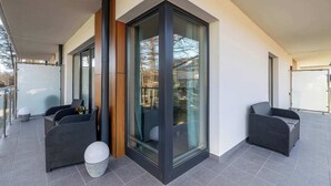 A modern outdoor patio with two wicker chairs, a glass door, and a tiled floor.