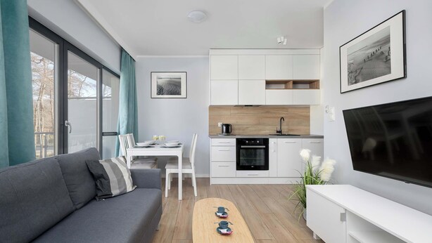 A modern living room with a sofa, a coffee table, a TV, and a kitchen area with cabinets and a stove.