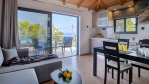 A modern room with a sofa, dining table, and chairs, a balcony with a view, and a kitchen area.