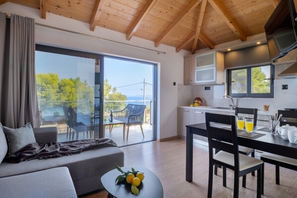 A modern room with a sofa, dining table, and chairs, a balcony with a view, and a kitchen area.