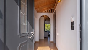 A hallway with a wooden ceiling, a grey door with a window, and an archway leading to a room with a view.