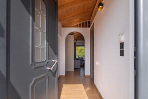 A hallway with a wooden ceiling, a grey door with a window, and an archway leading to a room with a view. - Villa with Sea View, Shared Garden & Wi-Fi (Lefkada)