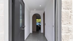 A hallway with a dark door, white walls, and a stone wall on the right. - Villa with Sea View, Shared Garden & Wi-Fi (Lefkada)