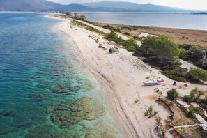 Una playa costera con aguas cristalinas, orilla arenosa y vegetación escasa.