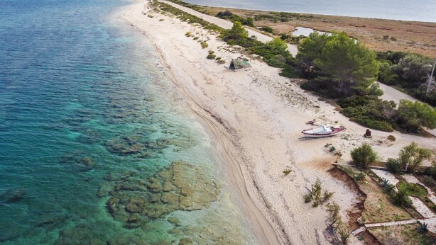 Une plage côtière aux eaux limpides, au rivage sablonneux et à la végétation clairsemée.