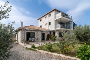 A two-story stone house with a balcony, outdoor seating, and a garden.