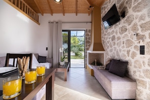A room with a stone wall, a wooden ceiling, a sofa, a table with glasses of orange juice, and a TV mounted on the wall.