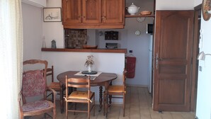 A compact kitchen with wooden cabinets, a dining table with chairs, and a small refrigerator. - Magnificent sea view 150 m from the beach, private domain of Gaou Benat (Bormes-les-Mimosas)