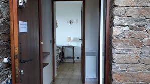 A hallway with a wooden door, a stone wall, a ceiling light, and a bed in the distance. - Magnificent sea view 150 m from the beach, private domain of Gaou Benat (Bormes-les-Mimosas)