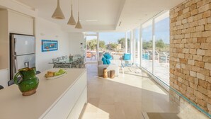 Eine moderne Küche mit einer zentralen Kochinsel, einem Essbereich mit Tisch und Stühlen sowie einem großen Fenster mit Blick ins Freie.