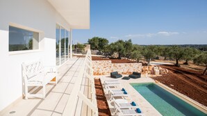 Ein moderner Poolbereich im Freien mit Liegestühlen, einer weißen Bank und einer Steinmauer.