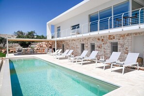 Ein moderner Poolbereich mit Liegestühlen, einer Steinwand und einem klaren, blauen Pool.