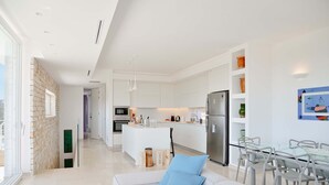 Eine moderne Küche mit weißen Schränken, einem Edelstahl-Kühlschrank und einem Essbereich mit einem Glastisch und Stühlen.