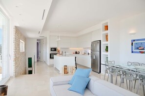 Eine moderne Küche mit weißen Schränken, einem Edelstahl-Kühlschrank und einem Essbereich mit einem Glastisch und Stühlen.