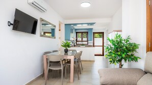 A modern living room with a flat-screen TV, a dining area with a table and chairs, and a large green plant.